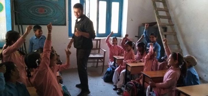 Karan teaching a classroom of children with their hands raised